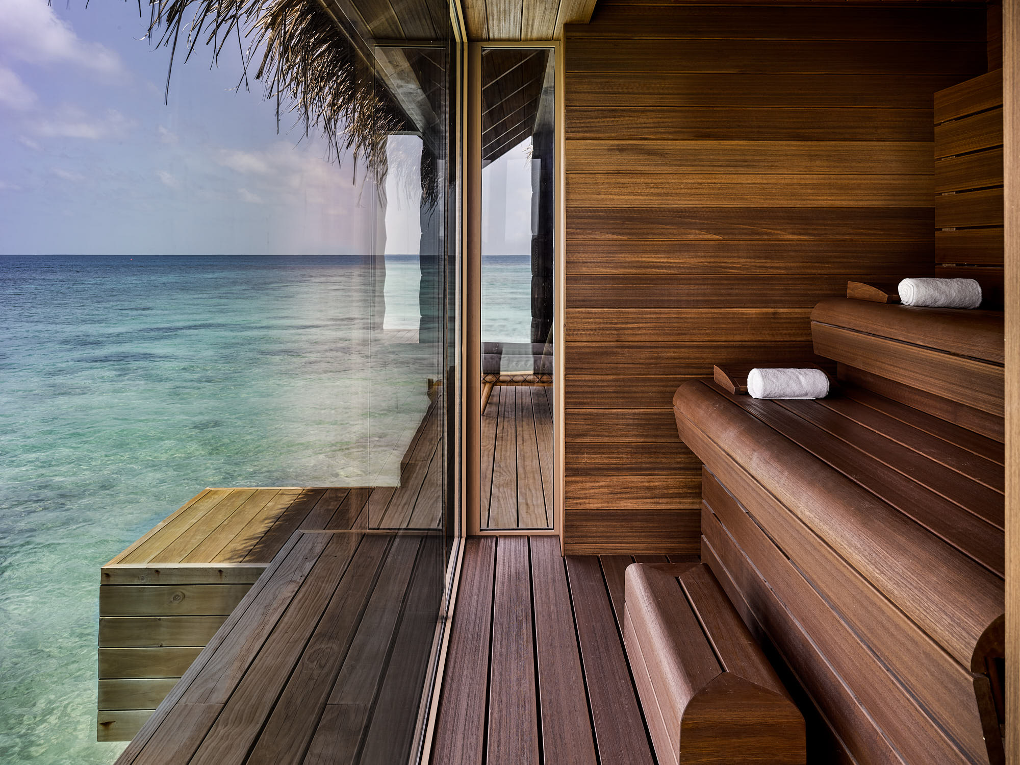 A sauna with a large glass wall looking out onto a calm sea and sunny sky