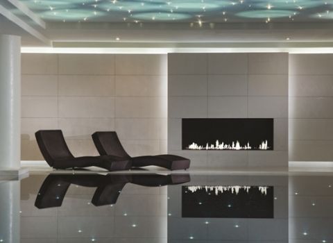 Two reclined seats next to a calm indoor pool, with a wide fireplace nearby.
