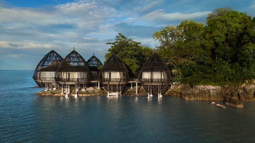 A group of pod-like rooms sit on stilts above a shoreline.