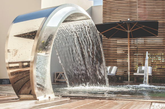 Large curved water feature pouring water into an outdoor pool